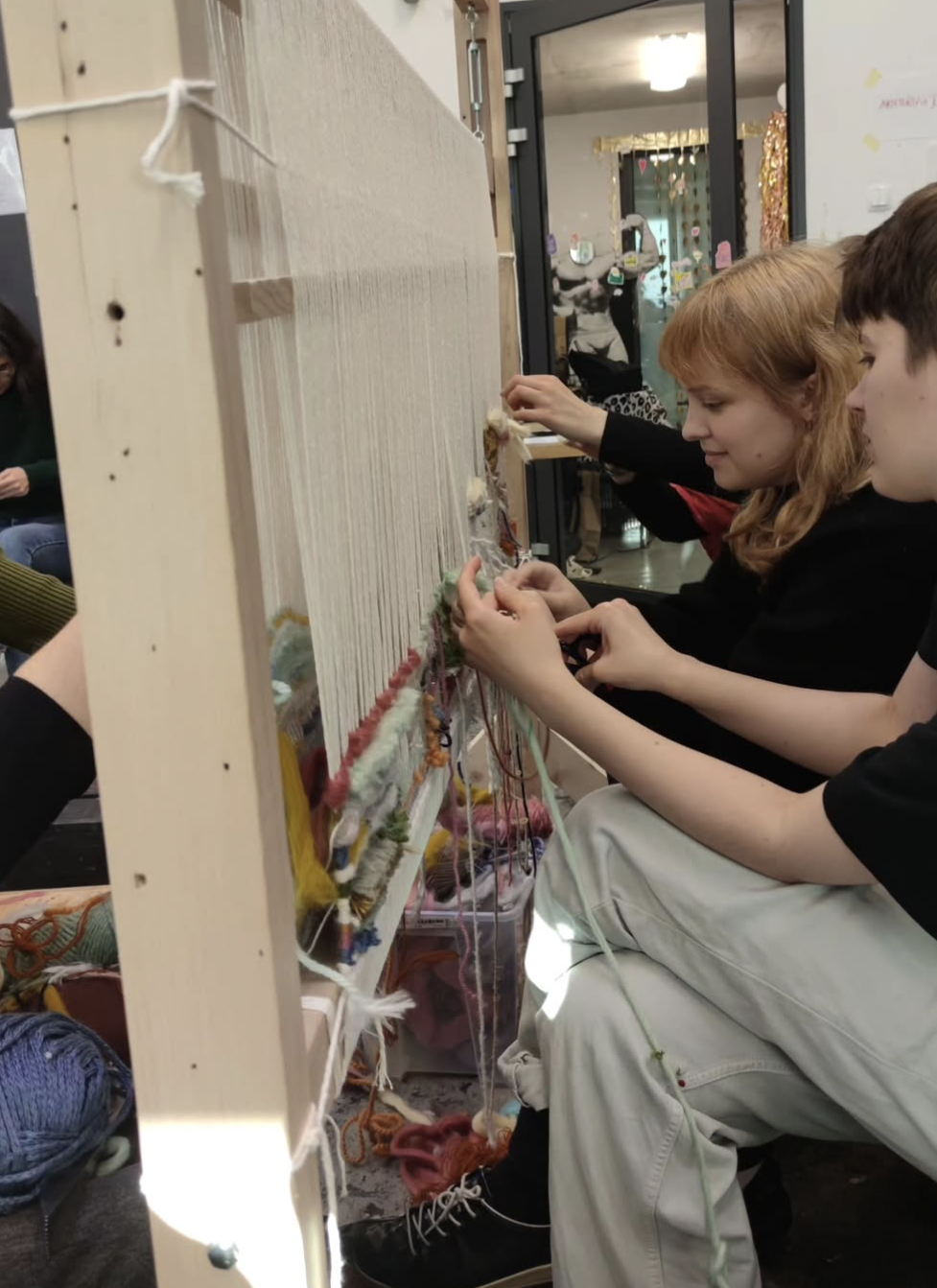 Workshop participants weaving together at a standing loom