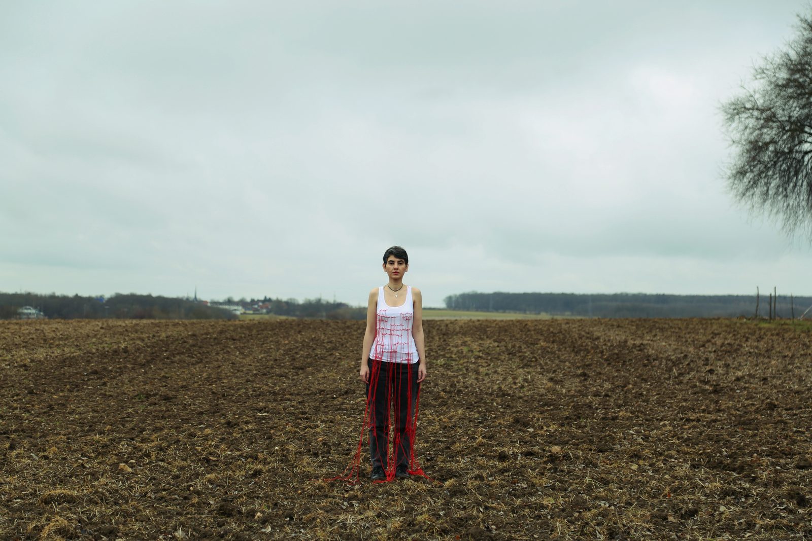 The artist standing in an open field wearing a dress laced with red thread