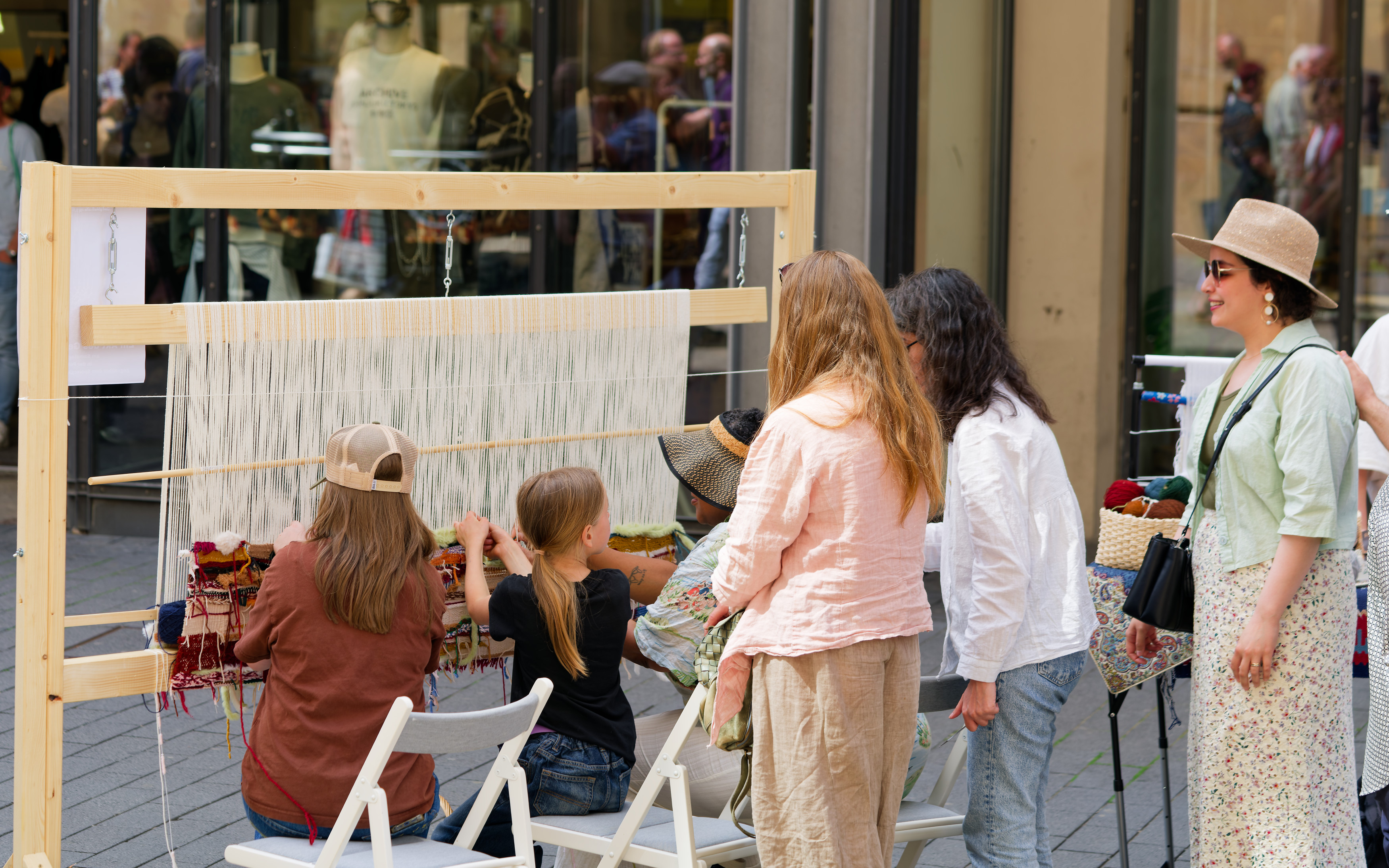 Participants weaving together at a wooden loom outdoors