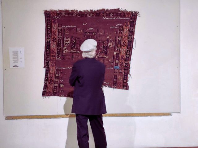 A visitor looking closely at the worn carpet on the gallery wall