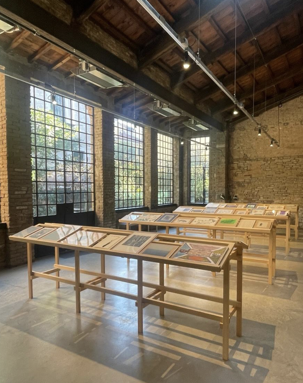Installation views of framed artworks displayed on wooden tables in a gallery